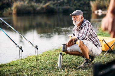 Olgun bir adam kampta tatlı suda balık tutarken içki içiyor..
