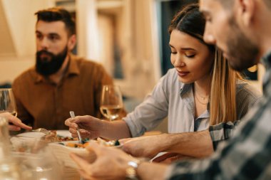 Group of friends having dinner together at dining table. Focus is on woman. 