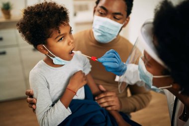 African American boy sitting in father's lap while going through PCR testing at home due to COVID-19 pandemic. 