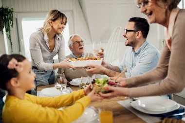 Cheerful multi-generation family having lunch together at home. Women are serving food. 