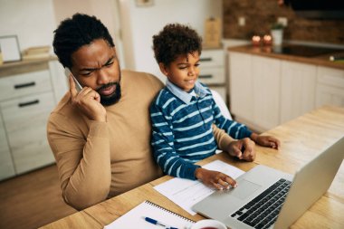 African American stay at home father communicating on mobile phone while his small son is sitting on his lap.