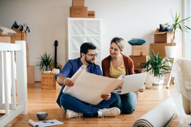 Happy couple going through housing plans and using computer while relocating into a new home. 