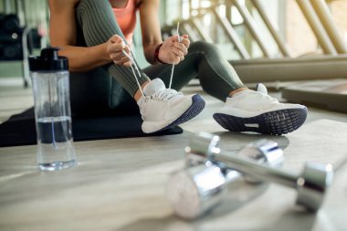 Unrecognizable female athlete tying shoelace while preparing for sports training in a gym. 