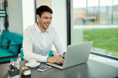 Happy businessman working on laptop while siting in a cafe. 