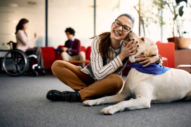 Happy entrepreneur embracing her Labrador therapy dog and having fun in the office. clipart