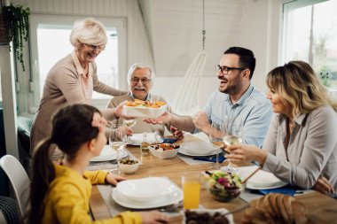 Happy multi-generation family having lunch together at home. Senior woman is bringing food to the table. 