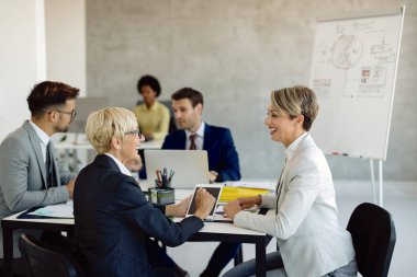 Happy mature businesswoman communicating with her younger colleague on a meeting in the office. 