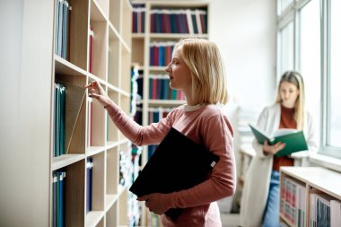 Smiling college student choosing book from bookshelf in a library.
