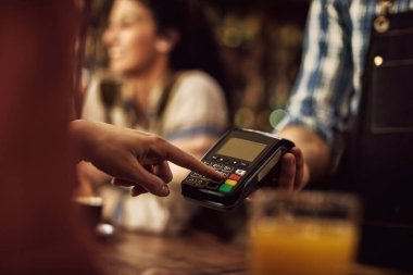 Close-up of customer entering pin on credit card reader while making payment in a pub. 
