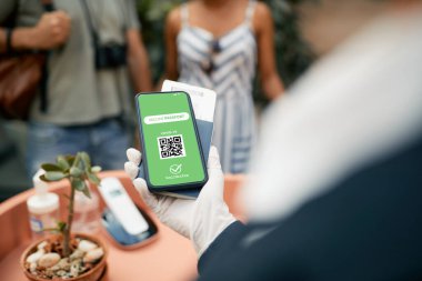 Close-up of receptionist checking digital certificate of coronavirus vaccination on smart phone during check-in of guests at the hotel.