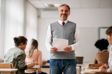 Portrait of happy mature professor during lecture in the classroom looking at camera. 