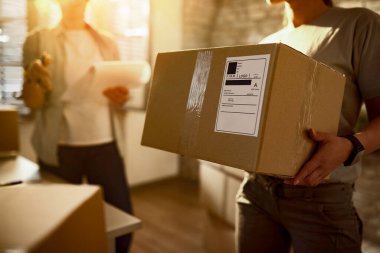 Unrecognizable delivery woman carrying a package while communicating with a colleague in the office. 