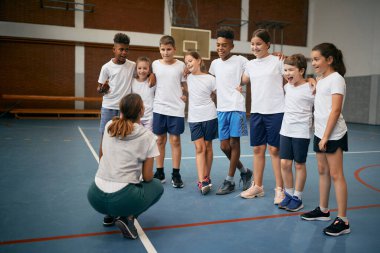 Group of happy elementary students with physical education teacher during a class at school gym. 
