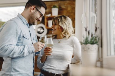Happy couple looking at each other while toasting with wine in the kitchen. 
