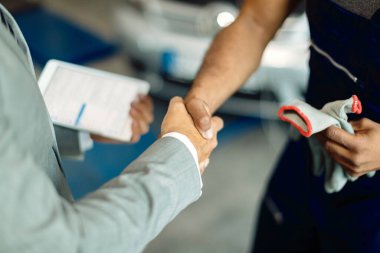 Close-up of auto repairman and businessman greeting in car workshop. 