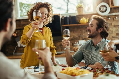 Group of young happy friends toasting with wine while having lunch together at home.