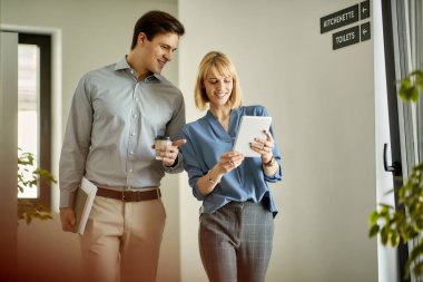 Happy businesswoman and her male colleague using touchpad while walking through lobby in the office.