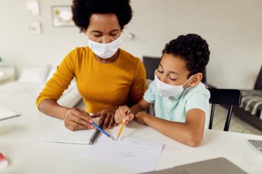 Black mother assisting her son in learning while homeschooling due to coronavirus epidemic. 