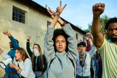 Young black woman participating in public demonstrations and showing peace gesture above her head.
