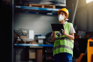 Female worker wearing protective face mask while working on digital tablet at distribution warehouse. 