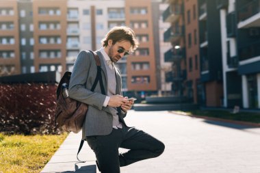 Young businessman using mobile phone and typing a message in the city. 