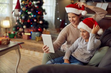 Happy mother and son having fun while using digital tablet and making video call on Christmas at home. 