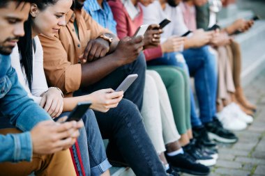 Young woman and her university friends using cell phones while relaxing outdoors.