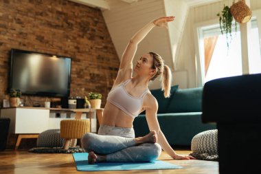 Kadın sporcu yerde oturuyor ve evde yoga egzersizleri yapıyor.. 