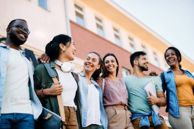 Low angle view of cheerful multi-ethnic students standing outdoors at the university.