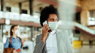 African American businesswoman wearing protective mask while communicating on mobile phone at the airport. 