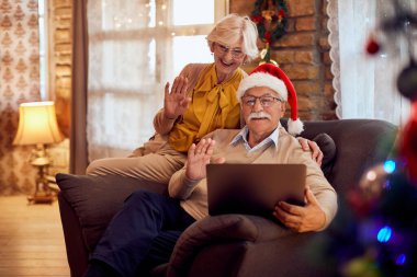 Happy senior couple using laptop and greeting someone during video call on Christmas.