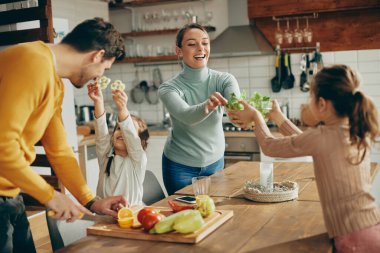 Happy parents and their daughters having fun while preparing meal together at home. 