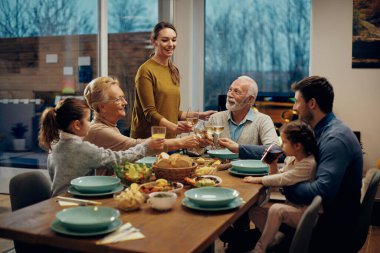 Happy extended family toasting while having lunch together in dining room.