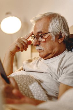 Mature man lying down in bed and reading a book. 