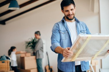 Happy man looking at wrapped picture while moving into a new home with his family. 