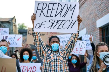 African American man wearing protective face mask while holding a freedom of speech placard during street demonstrations. 