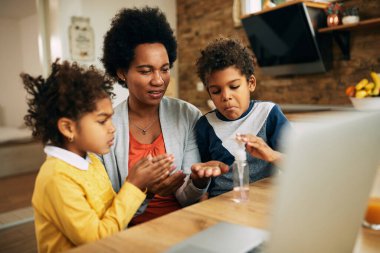 Mid adult black mother and her kids disinfecting their hands at home.