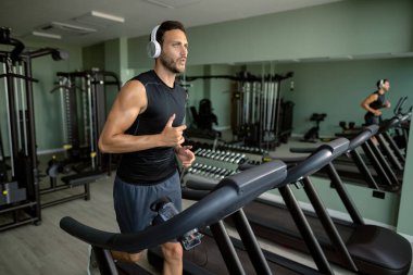 Determined athlete with headphones jogging on running track during sports training in health club. 