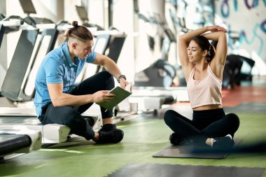 Genç sporcu kadın antrenörü spor salonunda egzersiz planlarını incelerken ısınıyor.. 