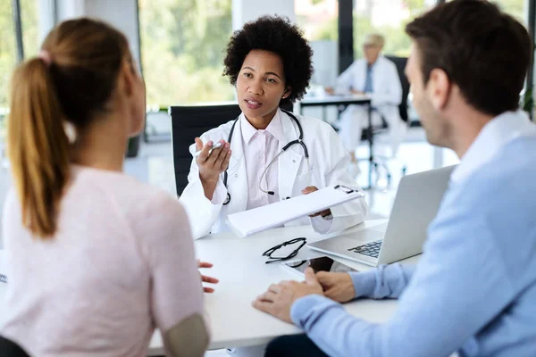 African American doctor communicating with a couple while analyzing their medical records during an appointment at doctor\'s office.
