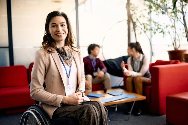 Portrait of smiling disabled businesswoman at corporate office looking at camera. Her colleagues are  in the background.