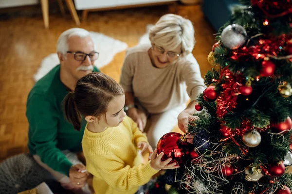 stock image High angle view of little girl and her grandparents decorating Christmas tree at home. 