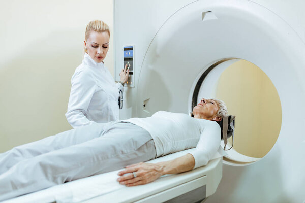 Senior woman undergoing on MRI scanner while doctor is supervising the procedure.