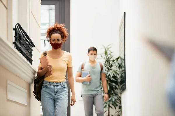 Distraught university student walking through a hallway and wearing protective face mask.