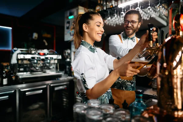 Young Happy Bartenders Pouring Beer Beer Tap While Working Pub — Stok fotoğraf