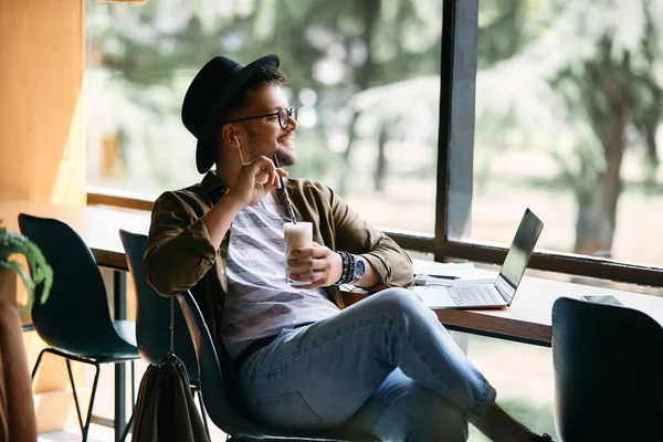 Male student day dreaming while taking a break from studying and drinking coffee in a cafe.