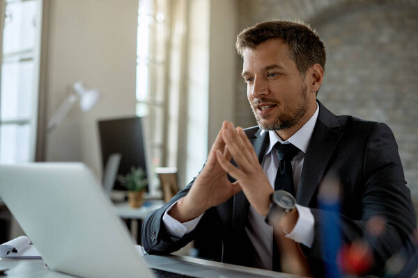 Smiling businessman reading an e-mail on laptop while working in the office. 