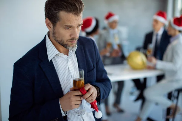 Pensive businessman feeling sad while his coworkes are celebrating in the background on New Year's party in the office.