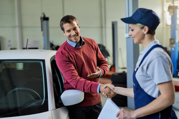 Satisfied customer handshaking with female mechanic in auto repair shop.