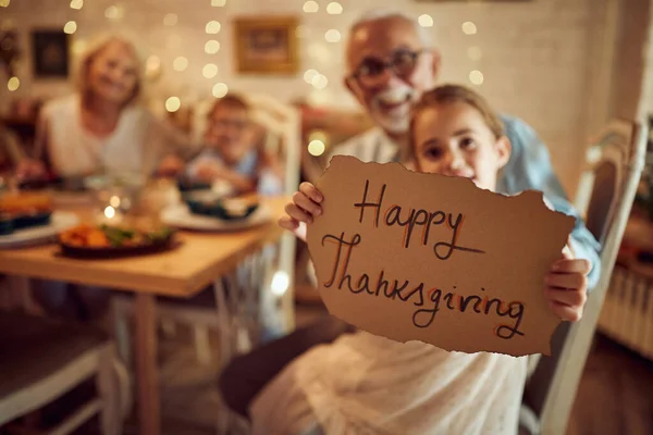 Close-up of girl holding Thanksgiving sign while having family dinner at home.